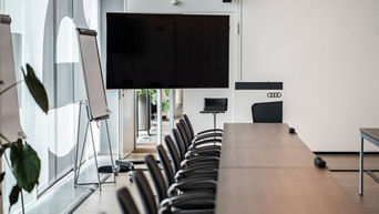 Konferenzraum mit einem langen Konferenztisch, Flipchart sowie einem großem Bild schirm und einem Rednerpult am Kopf des Tisches