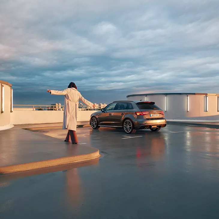 Kvinna balanserar över vattenpöl på parkering mot parkerad Audi