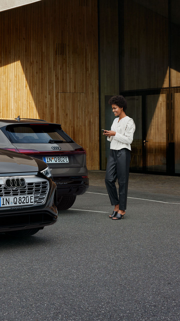 Vrouw met myAudi-app op haar mobiele telefoon loopt richting de Q8 e-tron