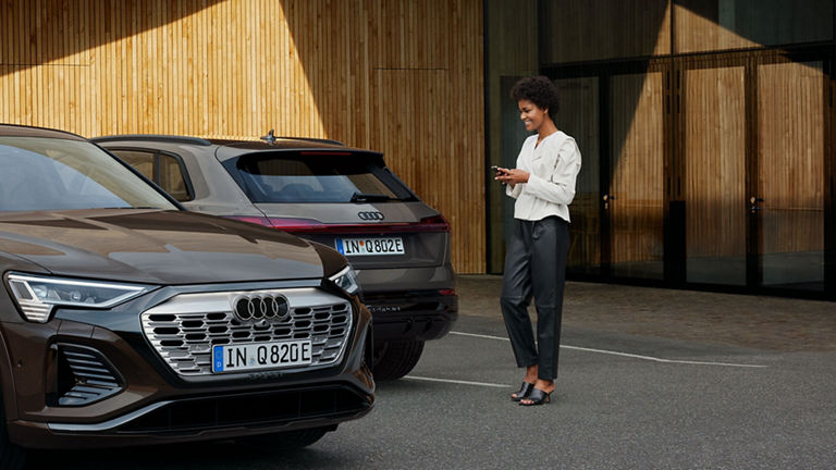 Kvinne med myAudi-appen på mobiltelefonen går mot Audi Q8 e-tron