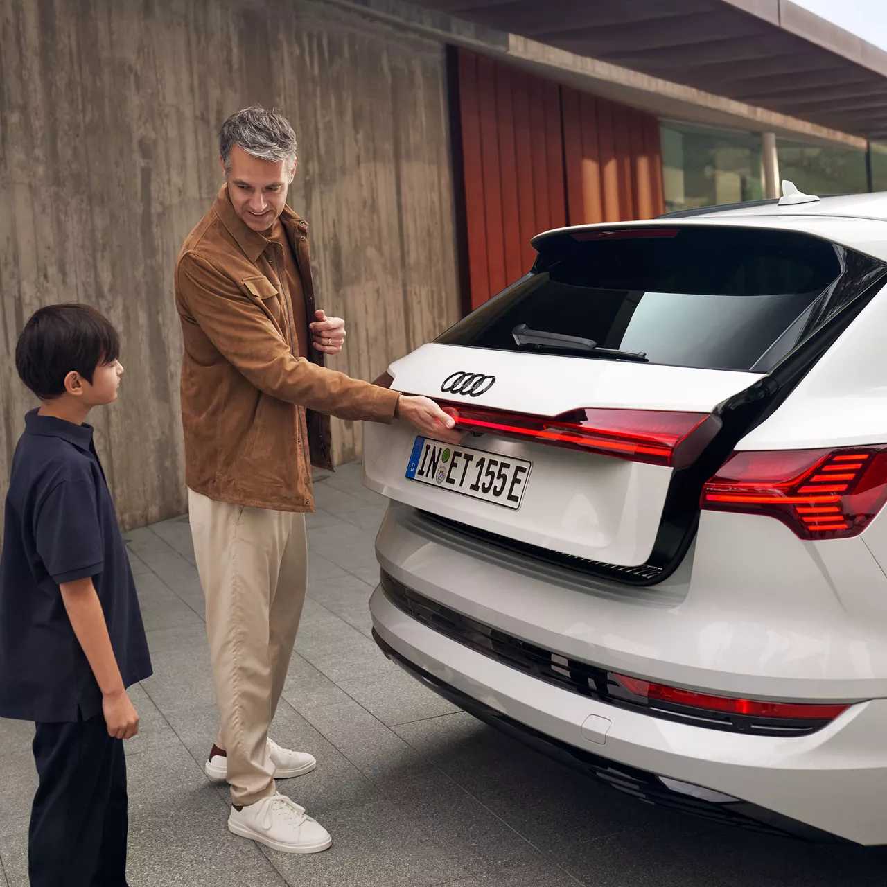 Un uomo apre il bagagliaio di un'Audi mentre un bambino lo guarda