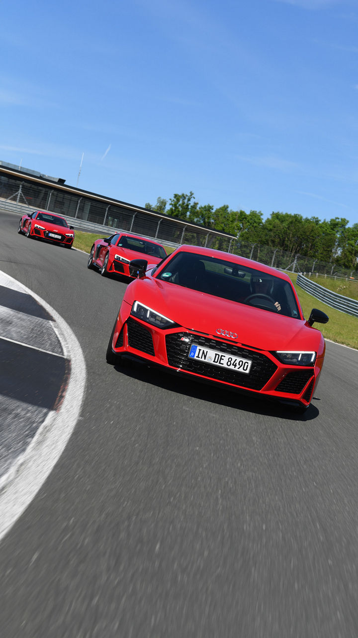 Three red Audi R8 Coupé V10 performance plus models drive head-on behind each other on a race track