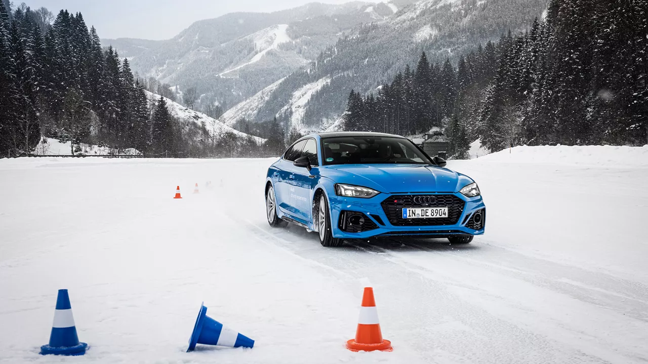 Hellblauer Audi RS 5 Sportback im Schnee in Saalbach, im Hintergrund Berge und Bäume