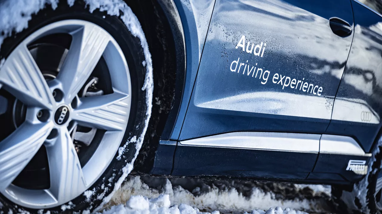 Dunkelblaues Audi Modell mit weißer Audi driving experience Aufschrift und Winterreifen von Pirelli im Schnee (Ansicht nur von Pirelli Reifen und Modellseite unten)