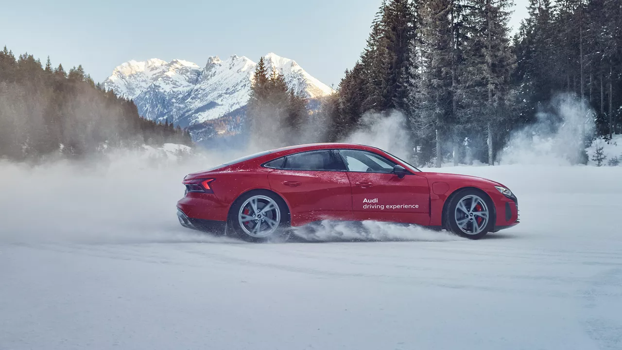 Red Audi model drives through a snowy landscape.