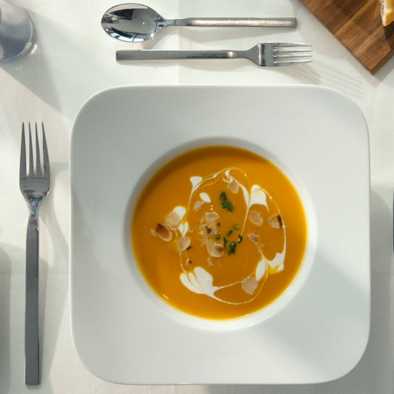 Ein weißer Teller, gefüllt mit einer orangefarbenen Tomatensuppe und Creme fraice und Kräutern
