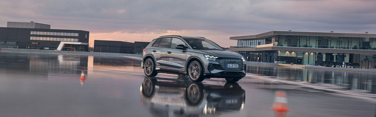 Grauer Audi Q4 e-tron fährt auf einer nassen Fahrbahn bei einem Training