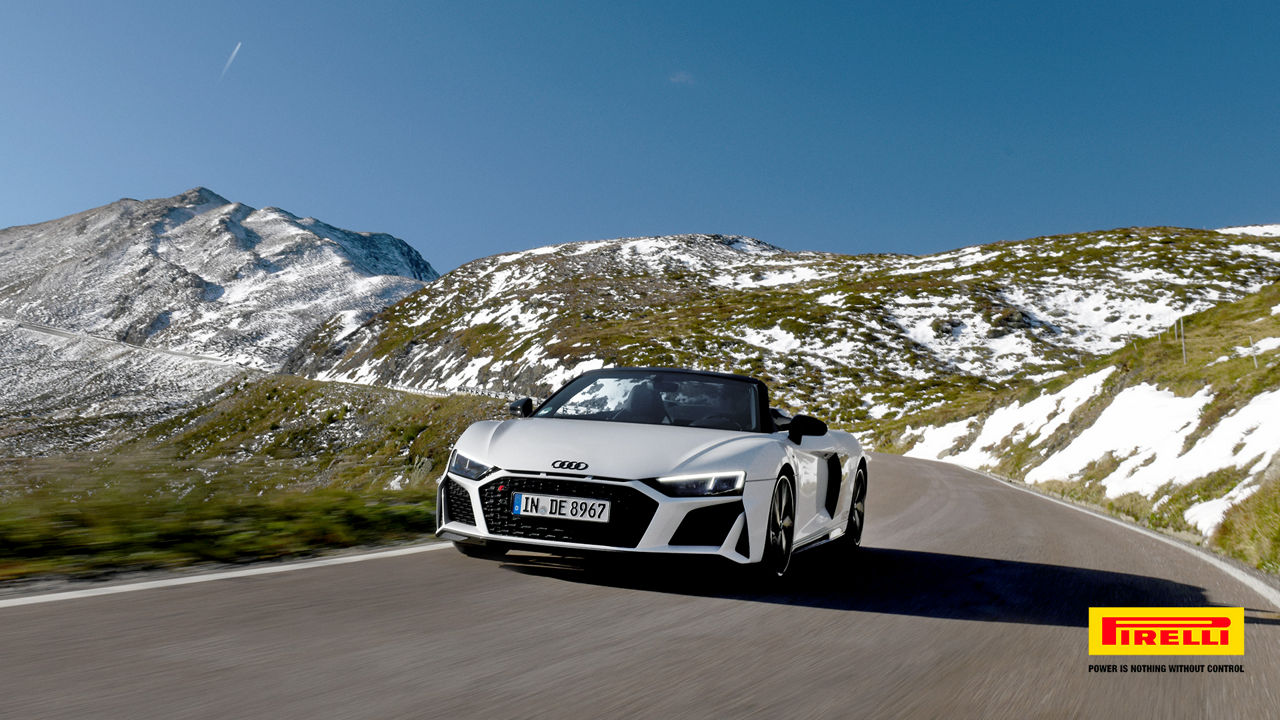 Weißer Audi R8 Spyder V10 performance quattro fährt auf einer Straße in den Bergen, die Berge sind mit Schnee bedeckt und der Himmel ist blau