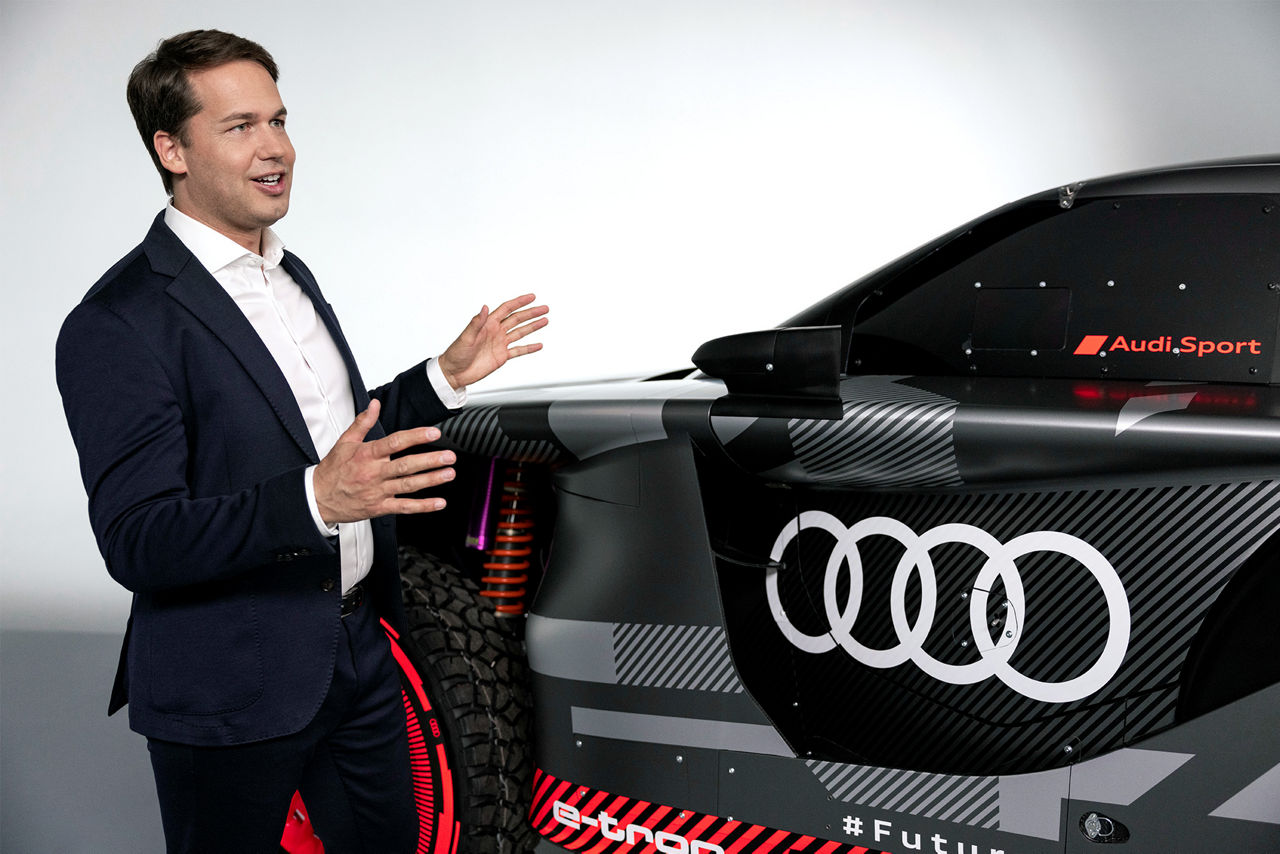 Julius Seebach à côté de l'Audi RS Q e-tron, gesticulant avec ses mains.