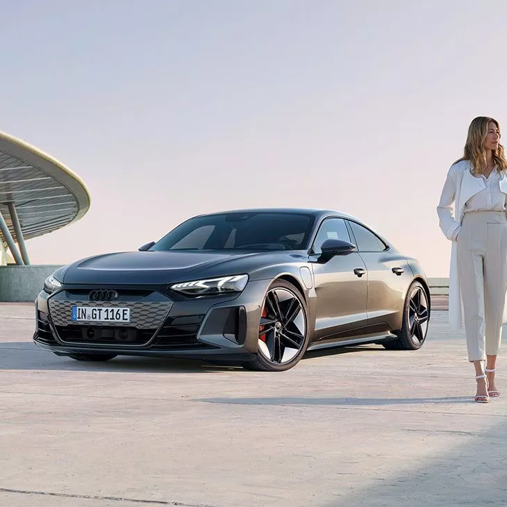 Elegant woman next to the Audi RS e-tron GT sports car on a concrete surface in front of futuristic architecture