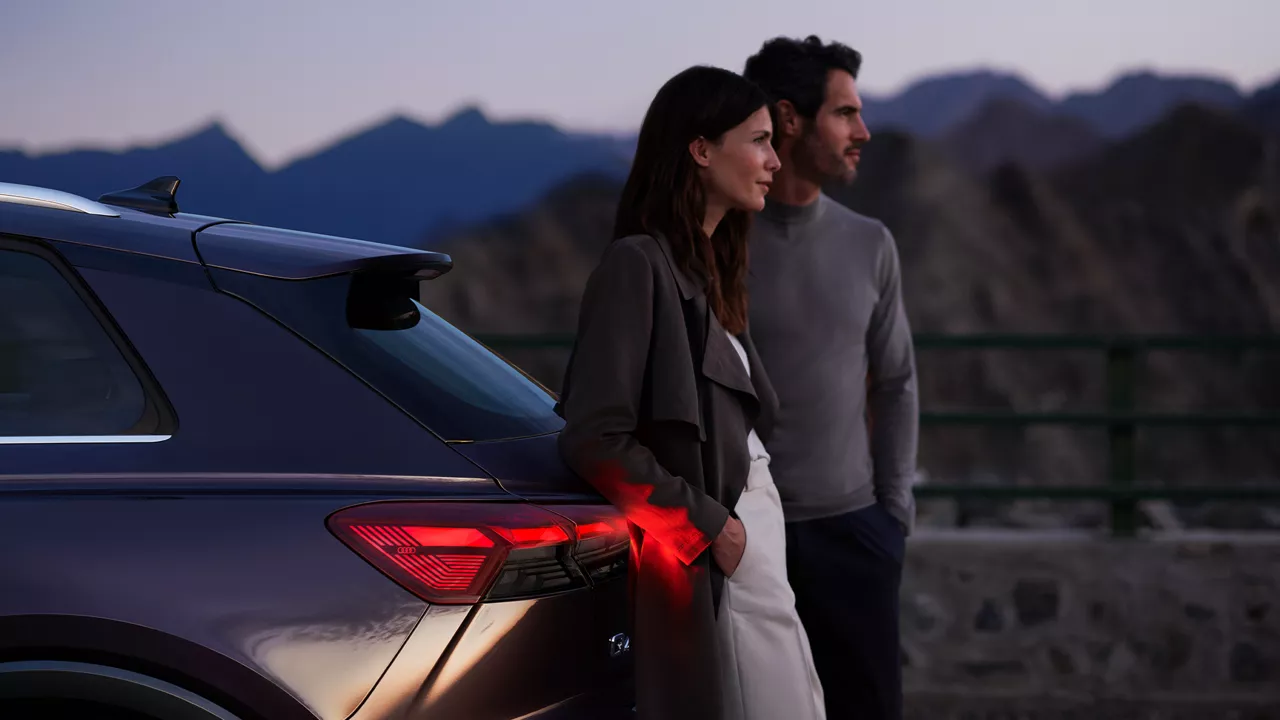 Un uomo e una donna appoggiati sul lato posteriore di un veicolo Audi.