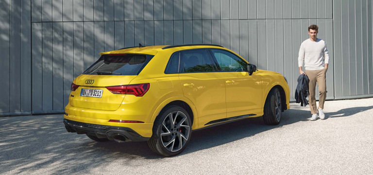 Audi RS Q3 i gult sett bakfra, foran en grå vegg med en mann på siden.