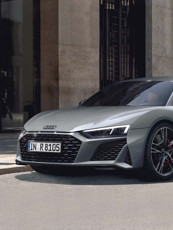 Side front view of the R8 Coupé V10 performance quattro in grey with black sideblades in front of a house