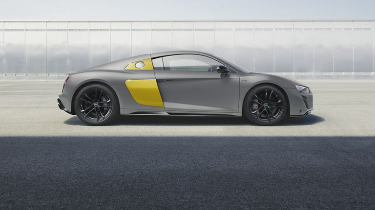 Seitliche Ansicht des R8 Coupé V10 performance quattro RWD mit gelben Sideblades vor einer Wand aus Metallplatten