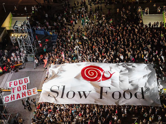 A crowd stands in front of a stage carrying a huge Slow Food banner.