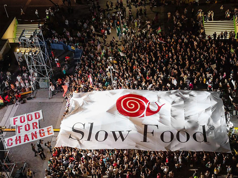 Tłum stoi przed sceną niosąc ogromny baner Slow Food.