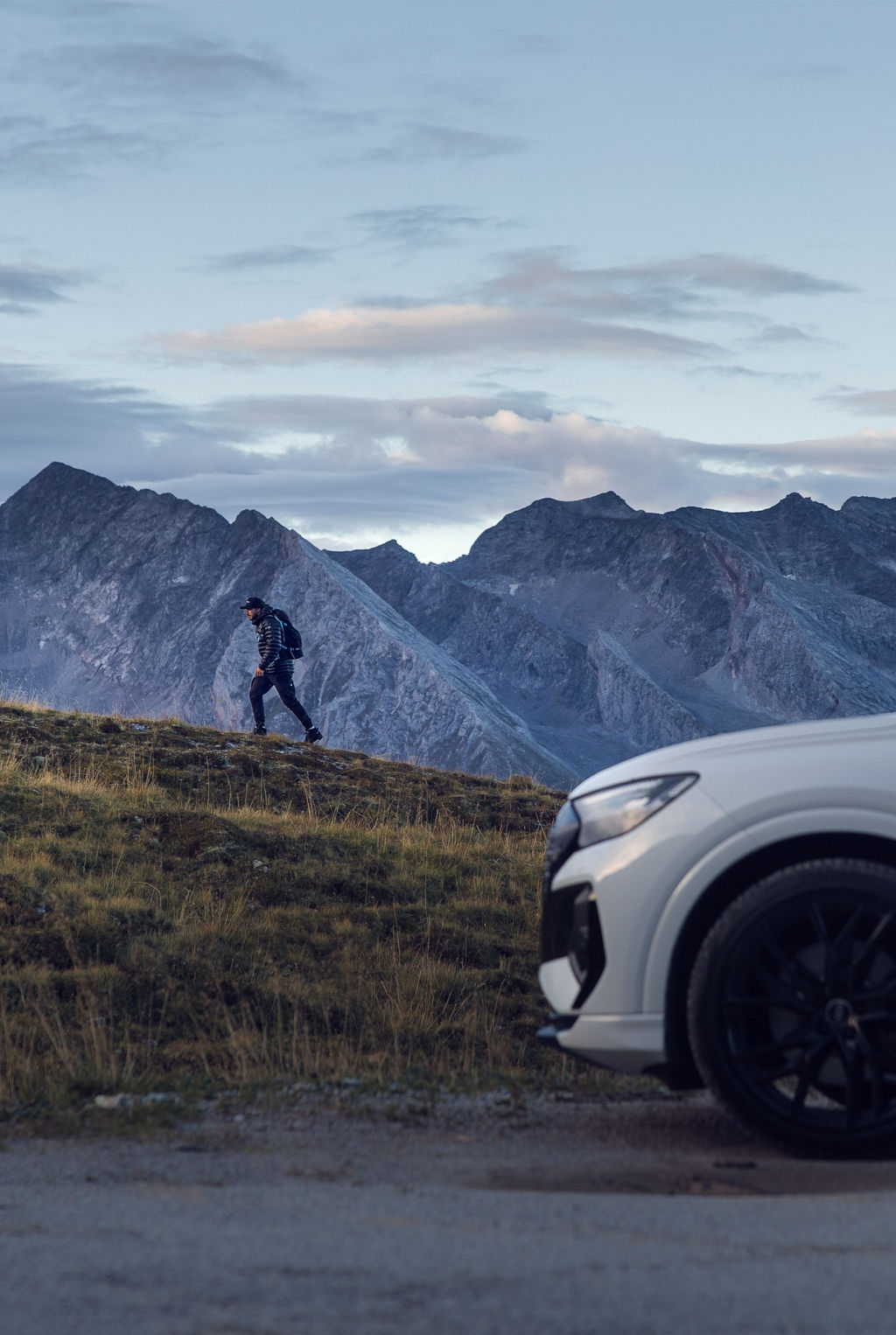 Den vita Audi Q4 e-tron står vid foten av berget som Tom Klocker vandrar upp för.