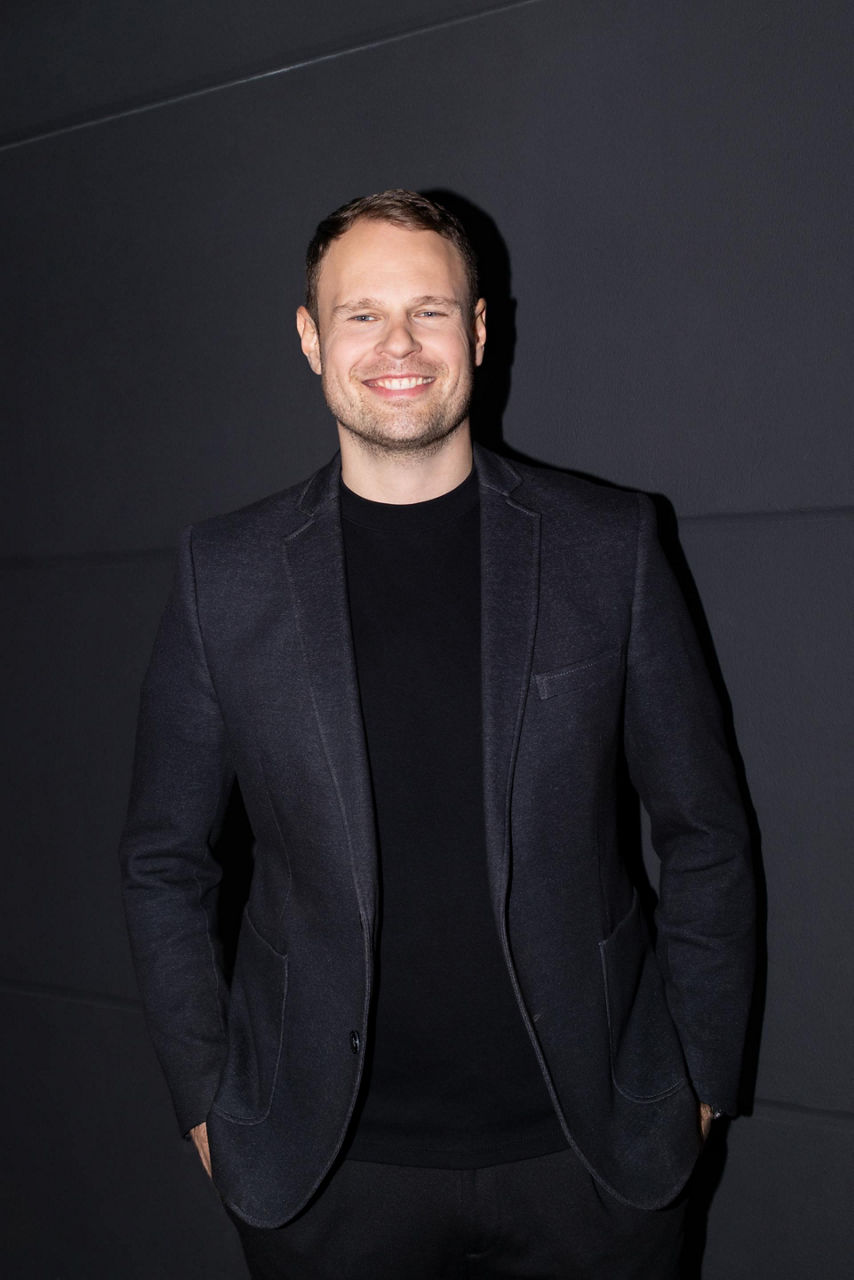 Portrettbilde av Andreas Ruf, teamleder hos Audi. Ruf står foran en mørk bakgrunn og har begge armene stukket ned i lommene på buksene sine.