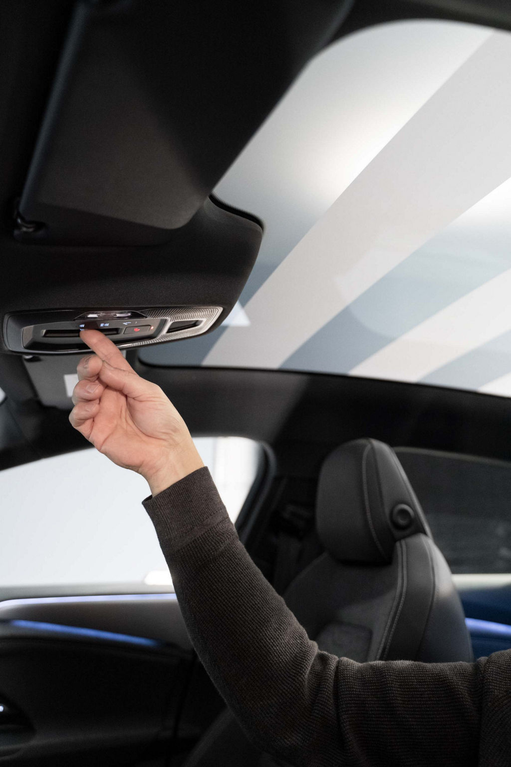 View of the interior through the driver's door of the Audi A6 Sportback e-tron. One hand reaches after the Control element in the headlining of the Audi. The panoramic roof can be seen in a striped pattern.