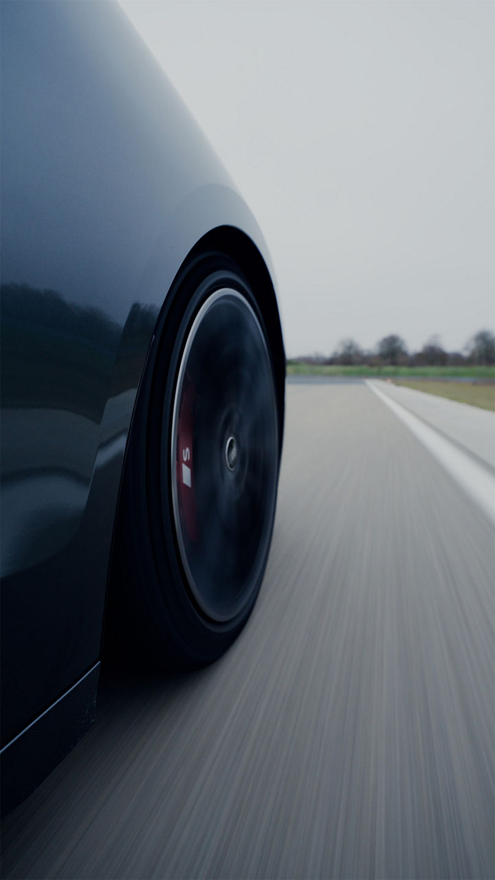 Nærbilde av et Audi S6 Avant e-tron fordekk i bevegelse på asfalt.