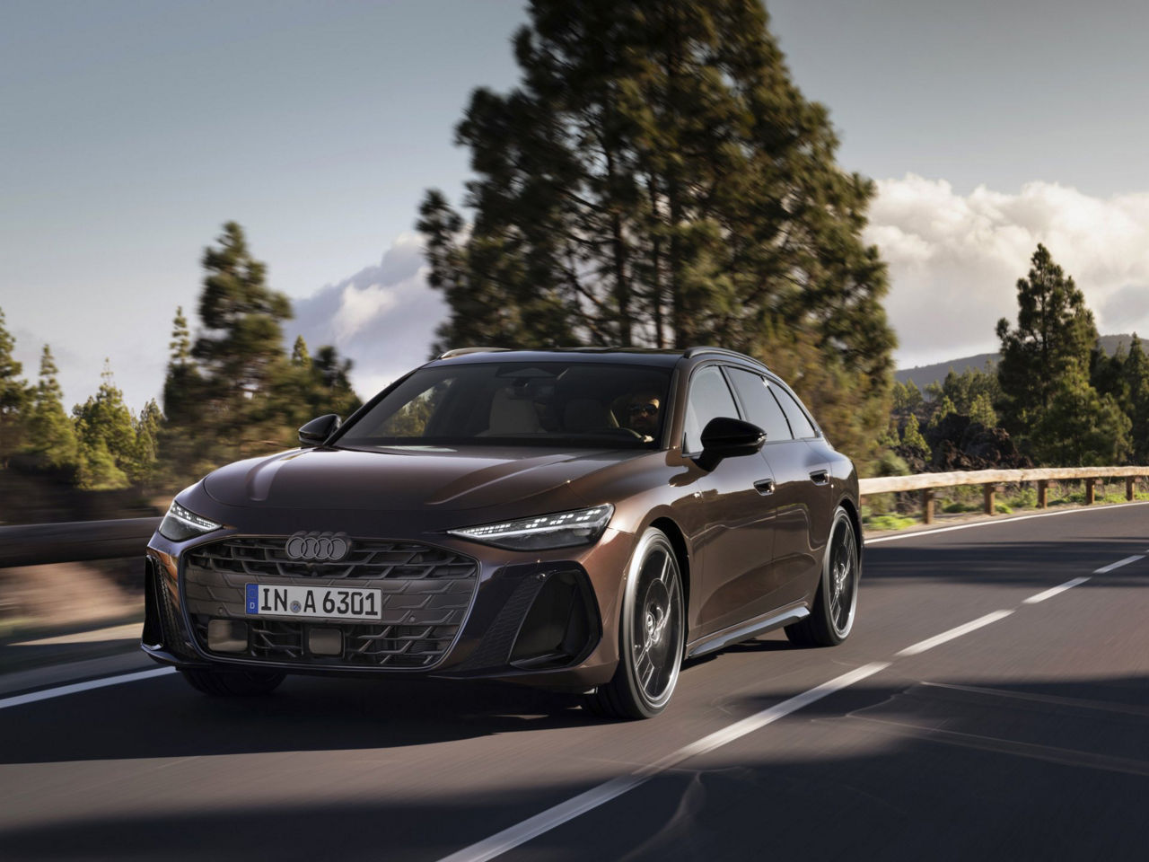 Frontansicht eines Audi A6 Avant, der eine Straße entlang fährt. Im Hintergrund ist eine Waldlandschaft zu erkennen.