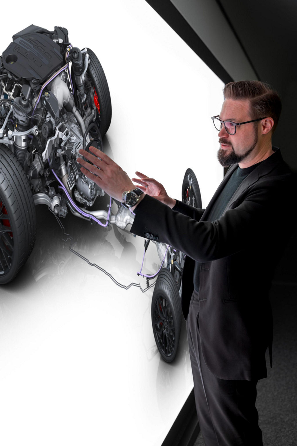 Eine Projektion an einer Powerwall zeigt schematisch den Antriebsstrang eines Audi A6. Matthias Honzen steht davor  und erklärt gestenhaft.