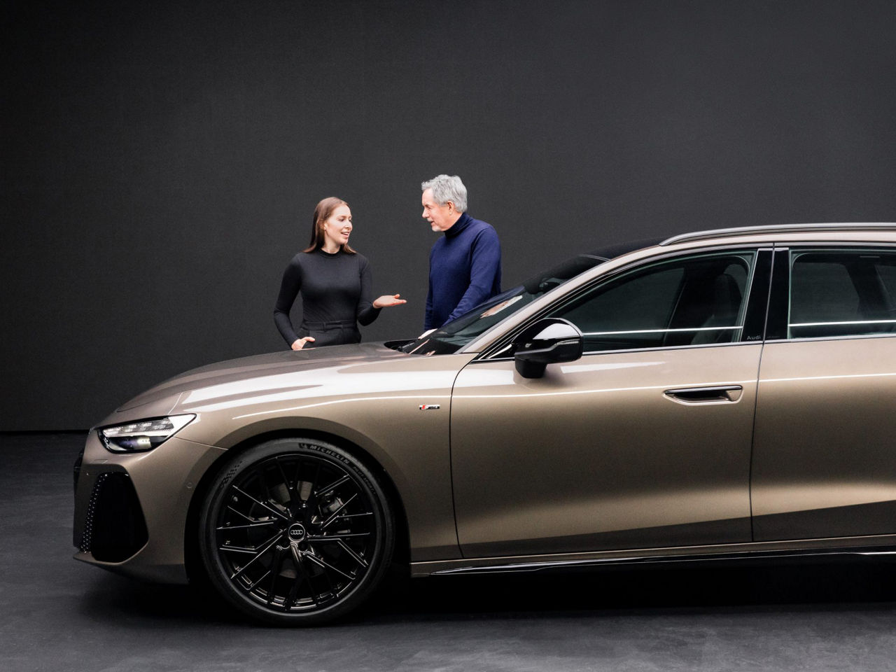 Annika Stößl und Trevor Hill stehen an der Fronthaube des Audi A6 Avant und unterhalten sich.