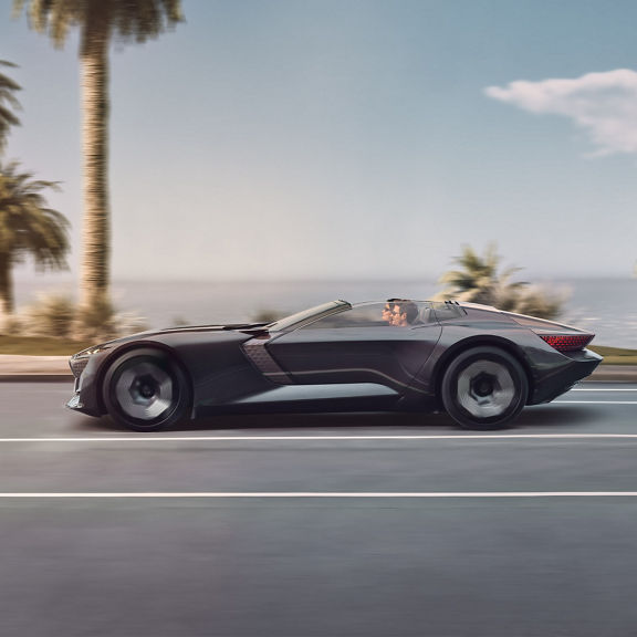 A side view of the open-top Audi skysphere concept driving fully automatically along a coastal road.