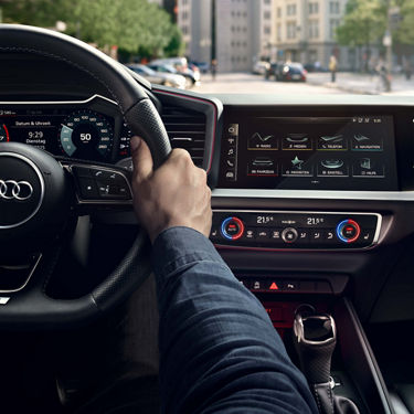 Fahrerhand am Lenkrad eines Audi A1 allstreet mit digitalem Tacho, Touchscreen-Menü und Klimabedieneinheit.