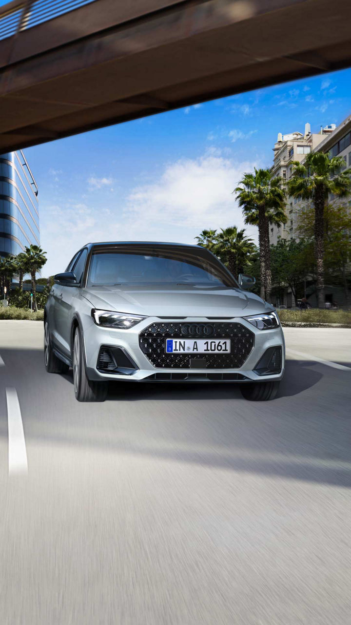 Frontansicht eines silbernen Audi A1 allstreet auf einer städtischen Straße mit Palmen und modernen Gebäuden im Hintergrund.