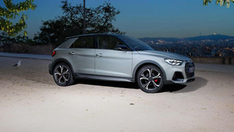 Silberner Audi A1 allstreet im Profil, geparkt auf heller Fläche mit nächtlicher Stadt im Hintergrund.