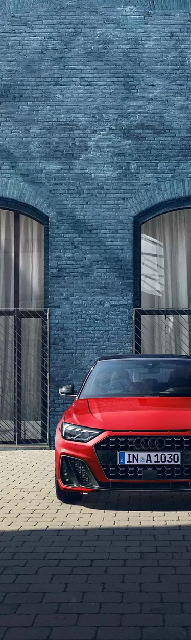 Roter Audi A1 frontal vor einer blauen Backsteinfassade mit großen Fenstern und hellem Vorhang.