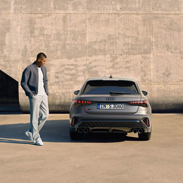 Rückansicht eines silbernen Audi S3 Sportback mit vier Auspuffrohren, daneben steht ein Mann.