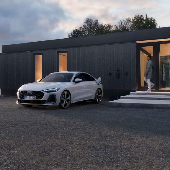 Audi A5 saloon e-hybrid charging in front of a house, with a man coming out of the door