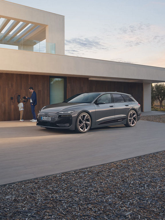 Audi A6 Avant e-tron vidd en laddstation. En person och ett barn står bredvid bilen.