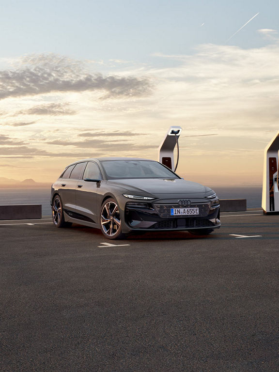 Audi A6 Avant e-tron vid en laddsation. En person står bredvid och ser ut över vattnet.