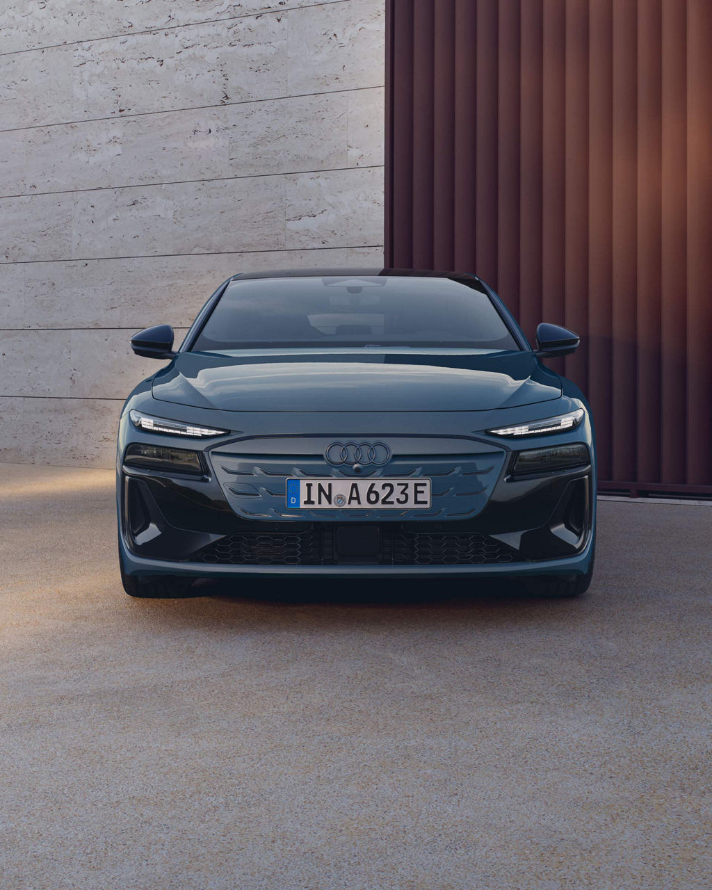 Frontansicht eines blauen Audi A6 Sportback e-tron vor Betonwand und vertikalem Holztor.