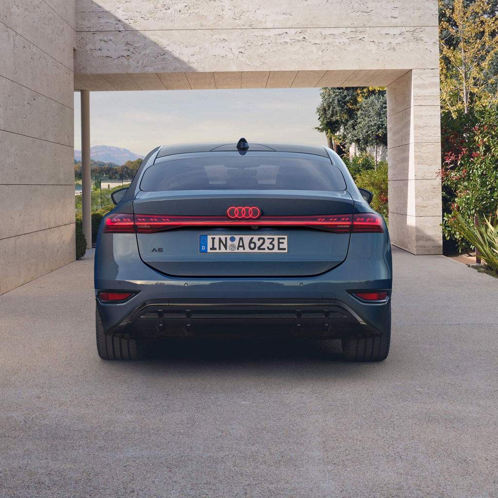 Heckansicht eines blauen Audi Sportback A6 e-tron mit leuchtendem Lichtband, unter Betonvordach.