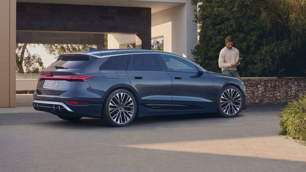 Ein dunkelblauer Audi S6 Avant e-tron von der Seite, ein Mann in heller Kleidung steht rechts daneben auf einer gepflasterten Einfahrt.