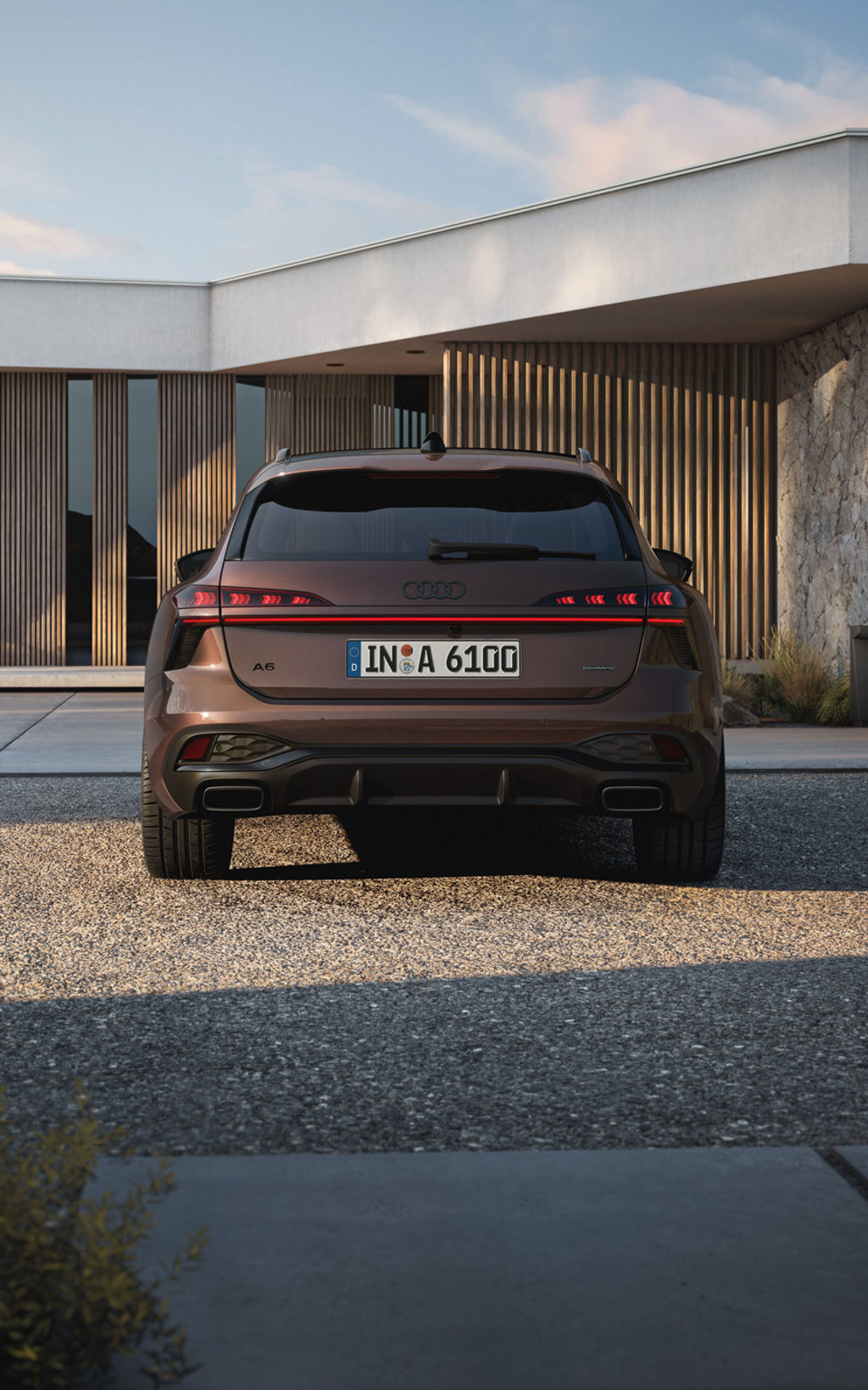 Brauner Audi A6 Avant Heckansicht, geparkt vor moderner Architektur mit Holz- und Steinfassade bei sonnigem Wetter.