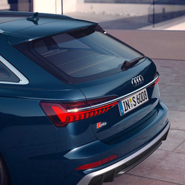 Seitliche Heckansicht eines blauen Audi S6 Avant TDI mit LED-Rückleuchten und S6-Badge, parkend auf heller Steinfläche.