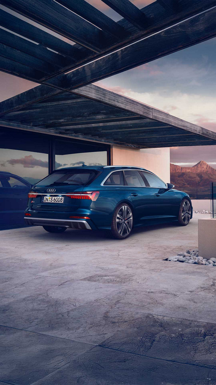 Heckansicht eines blauen Audi S6 Avant TDI vor modernem Gebäude mit Glasfront und Blick auf Berge im Hintergrund.