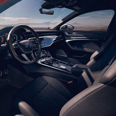 Modernes, schwarzes Interieur einer Audi S6 Limousine TDI mit digitalem Cockpit, Touchscreens und Blick auf weite Landschaft durch die Fenster.