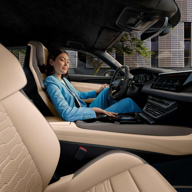 Eine Frau in einem blauen Anzug sitzt entspannt im Audi RS e-tron GT mit hellem Lederinterieur und digitalen Anzeigen.