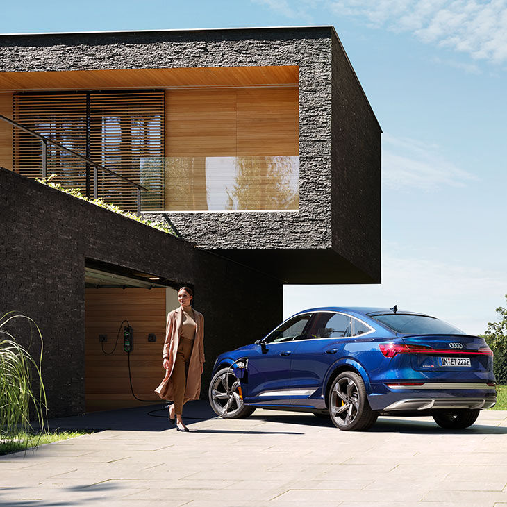 Dame står ved siden av en Audi Q8 Sportback e-tron utenfor hjemmet sitt.