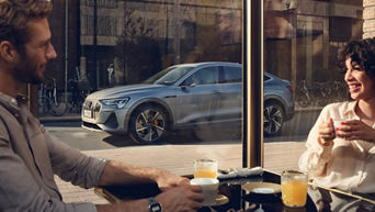 Kvinne og mann på cafe med Audi e-tron Sportback i bakgrunnen.