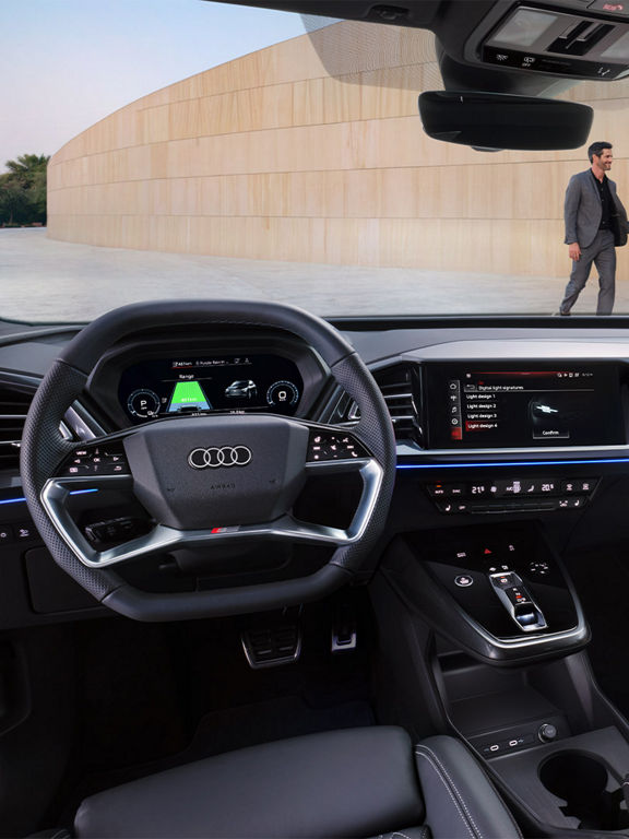 Primo piano del cockpit digitale dell’Audi Q4 e-tron con tachimetro, indicatore dello stato della batteria, data e ora. Il display mostra un’autonomia residua di 481 km e riproduce la canzone “Purple Rain”. Nella console centrale è visibile una selezione di funzioni luminose.