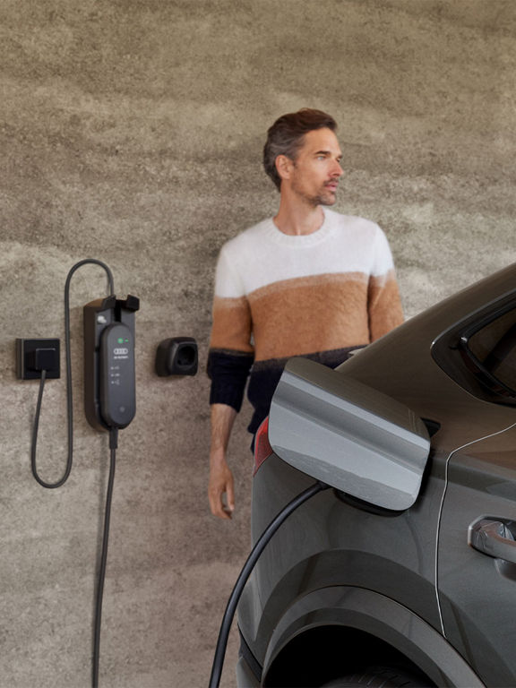 Audi Q6 Sportback e-tron laddas hemma, en man syns i bakgrunden