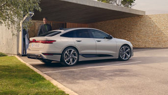 A6 Sportback e-tron  von der Seite hängt an einer Ladestation vor einem Haus