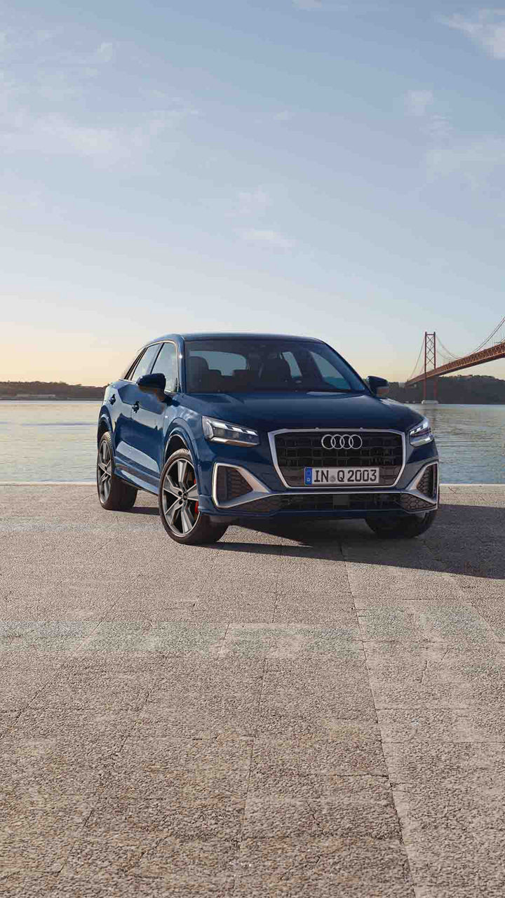 Mujer sentada mirando el río al lado de un Audi Q2 azul